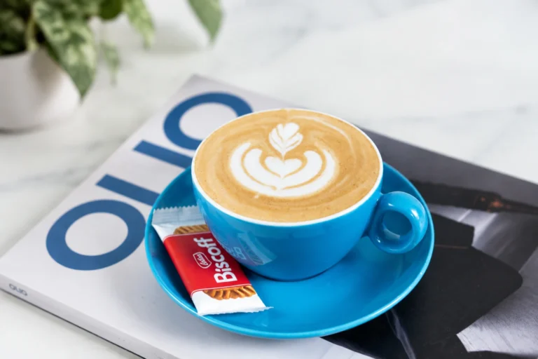 Hot latte art in blue cup with Biscoff biscuit on magazine: best coffee in Singapore.